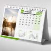A desk calendar for January, with a green border and a nature photo of a serene sunset over a body of water with reeds