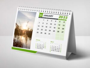A desk calendar for January, with a green border and a nature photo of a serene sunset over a body of water with reeds